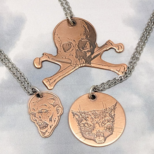 Three copper pendants with Halloween theme. Skull and crossbone, demen head, cat head