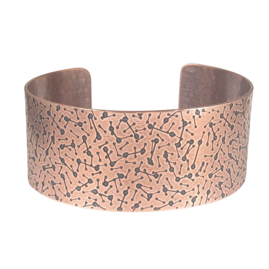 copper cuff covered in lines with dots on the ends to represent a meteor design