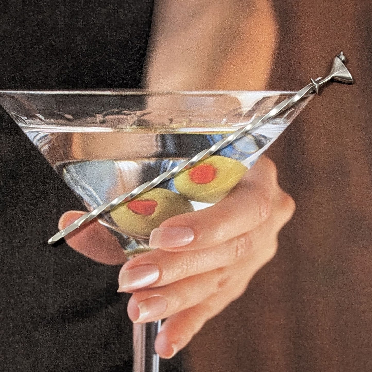 Sterling silver cocktail pick. At the top is a silver martini glass with a single olive.