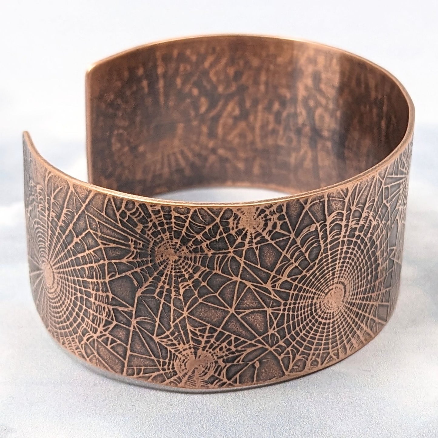 Wide copper cuff bracelet with impressed pattern of various sizes of spiderwebs