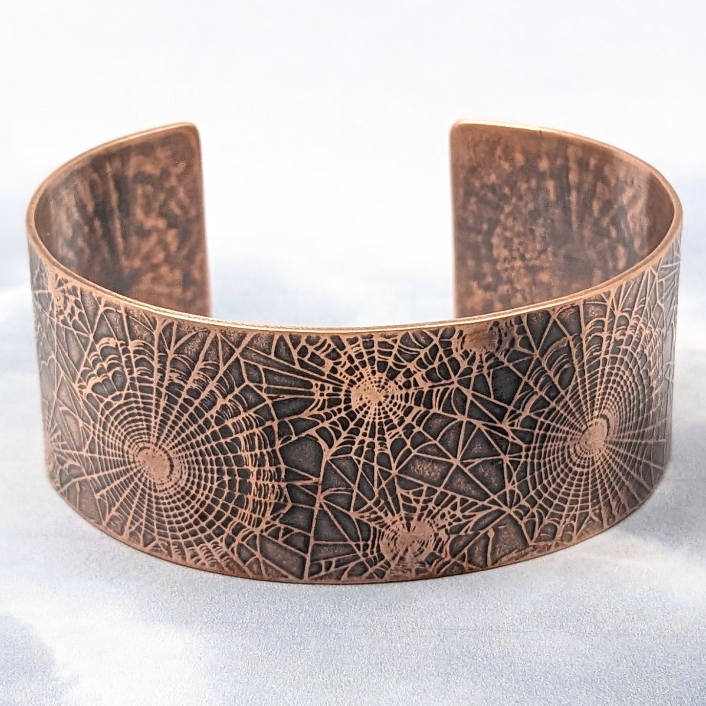 Wide copper cuff bracelet with impressed pattern of various sizes of spiderwebs