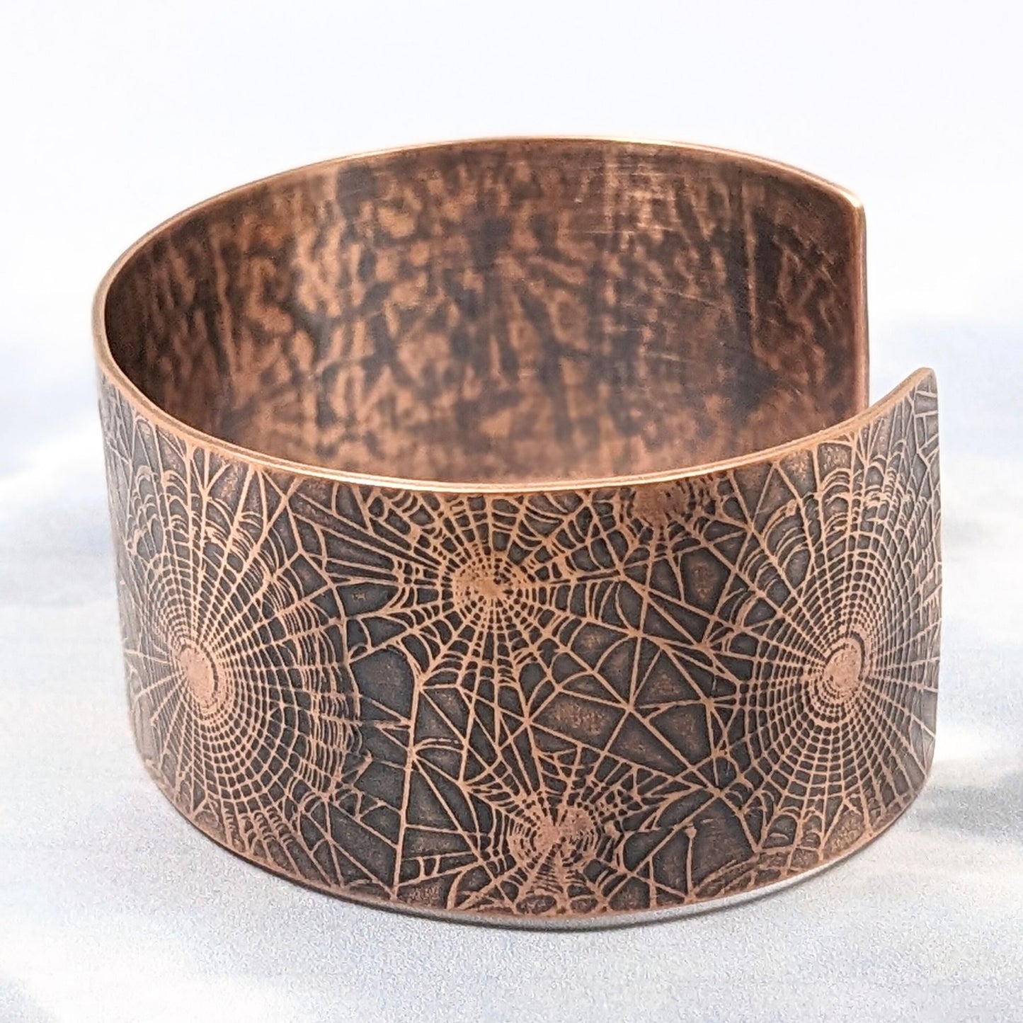 Wide copper cuff bracelet with impressed pattern of various sizes of spiderwebs