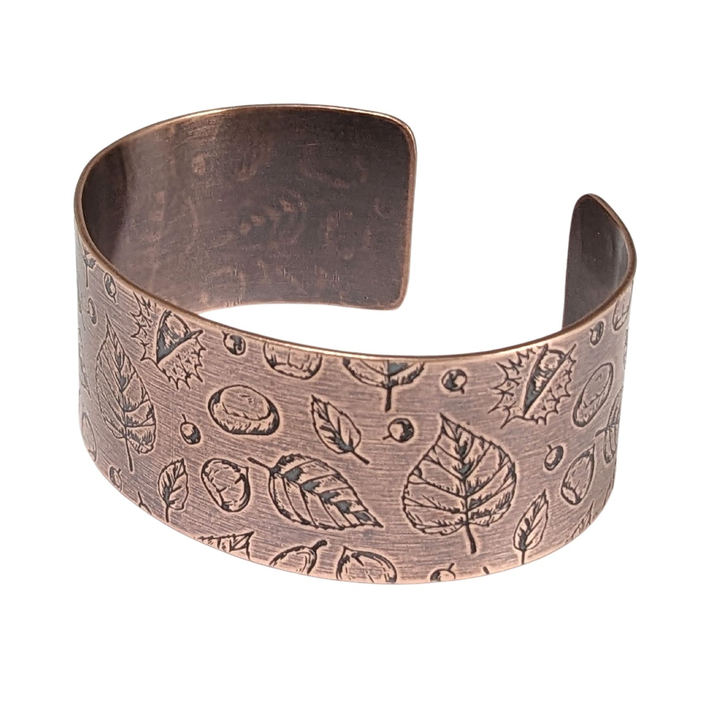A copper cuff bracelet covered in a pattern of fall leaves and nuts