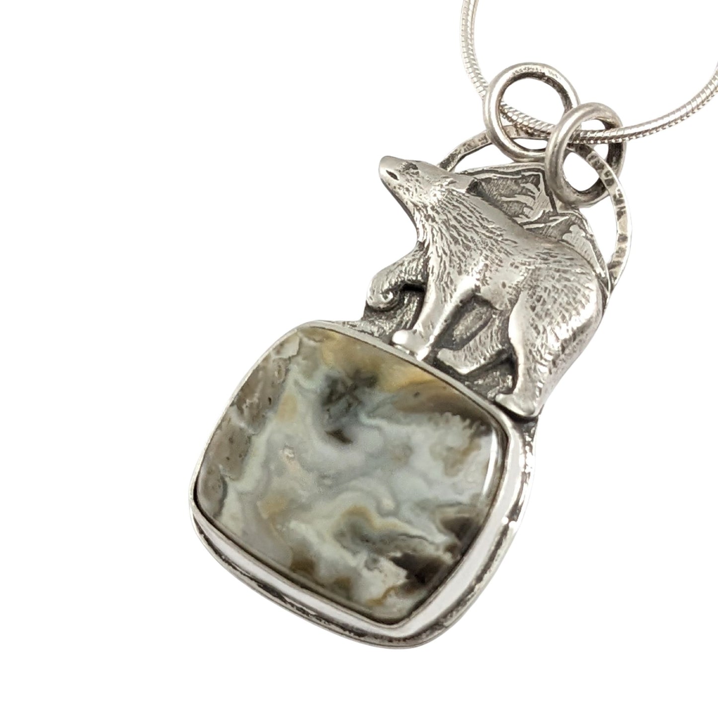 Sterling silver pendant. The top half is a bear walking against a background of mountains, the bottom half is a cabochon that looks like river rapids.