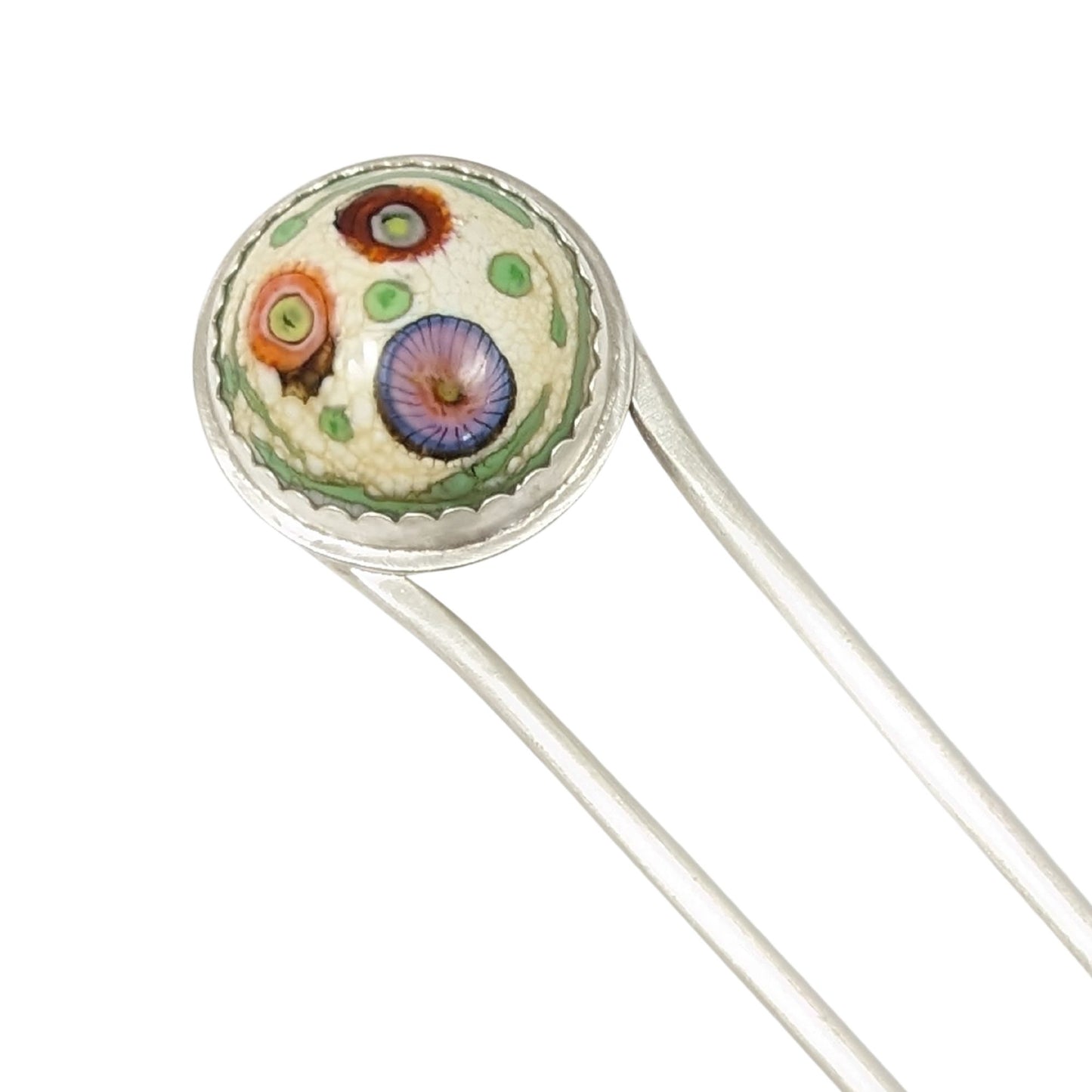 Sterling silver hair fork with a round lampwork glass stone at the top. The glass is pale yellow with ribbons of green around the edge and three abstract forms that look like flowers - one red, one orange, and one blue/pink.