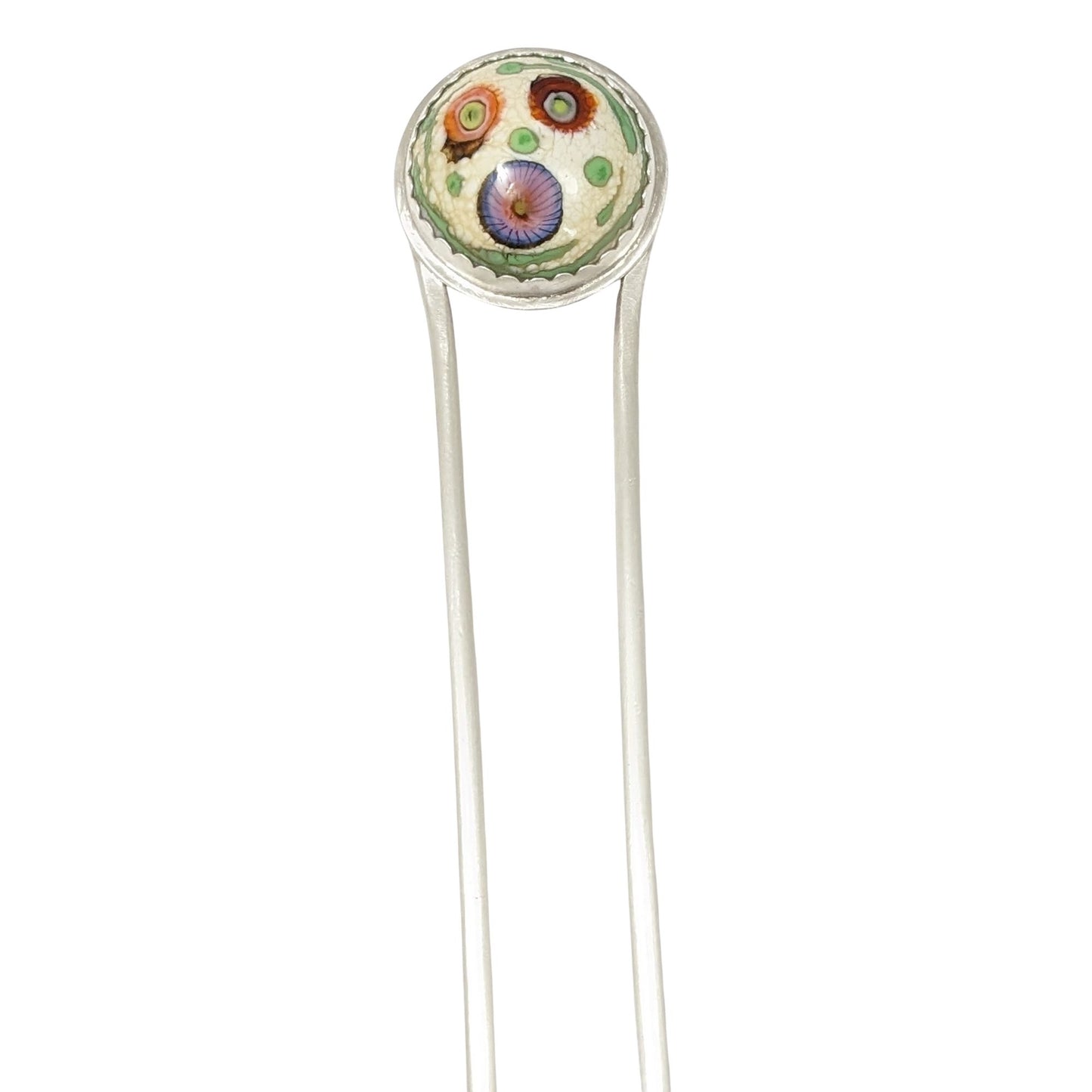 Sterling silver hair fork with a round lampwork glass stone at the top. The glass is pale yellow with ribbons of green around the edge and three abstract forms that look like flowers - one red, one orange, and one blue/pink.