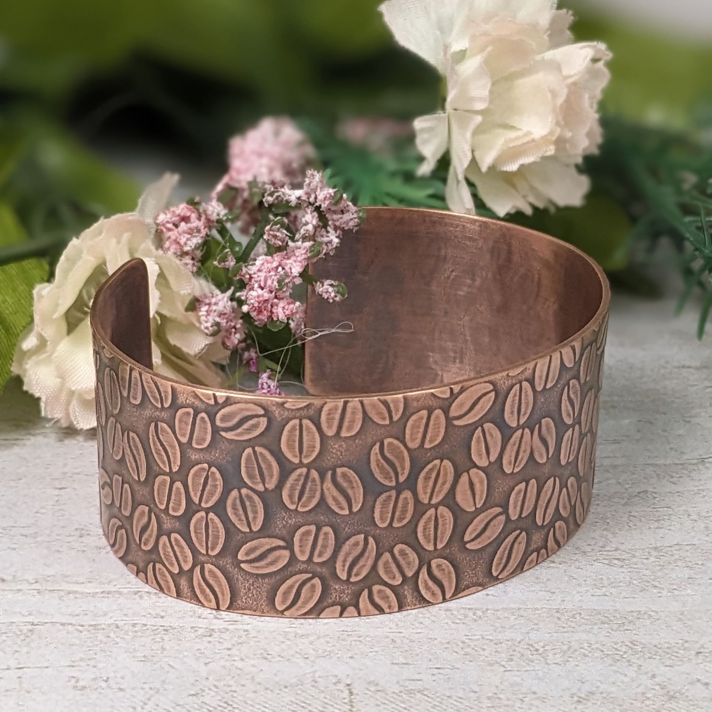 Copper cuff bracelet covered with impressed design of coffee beans.