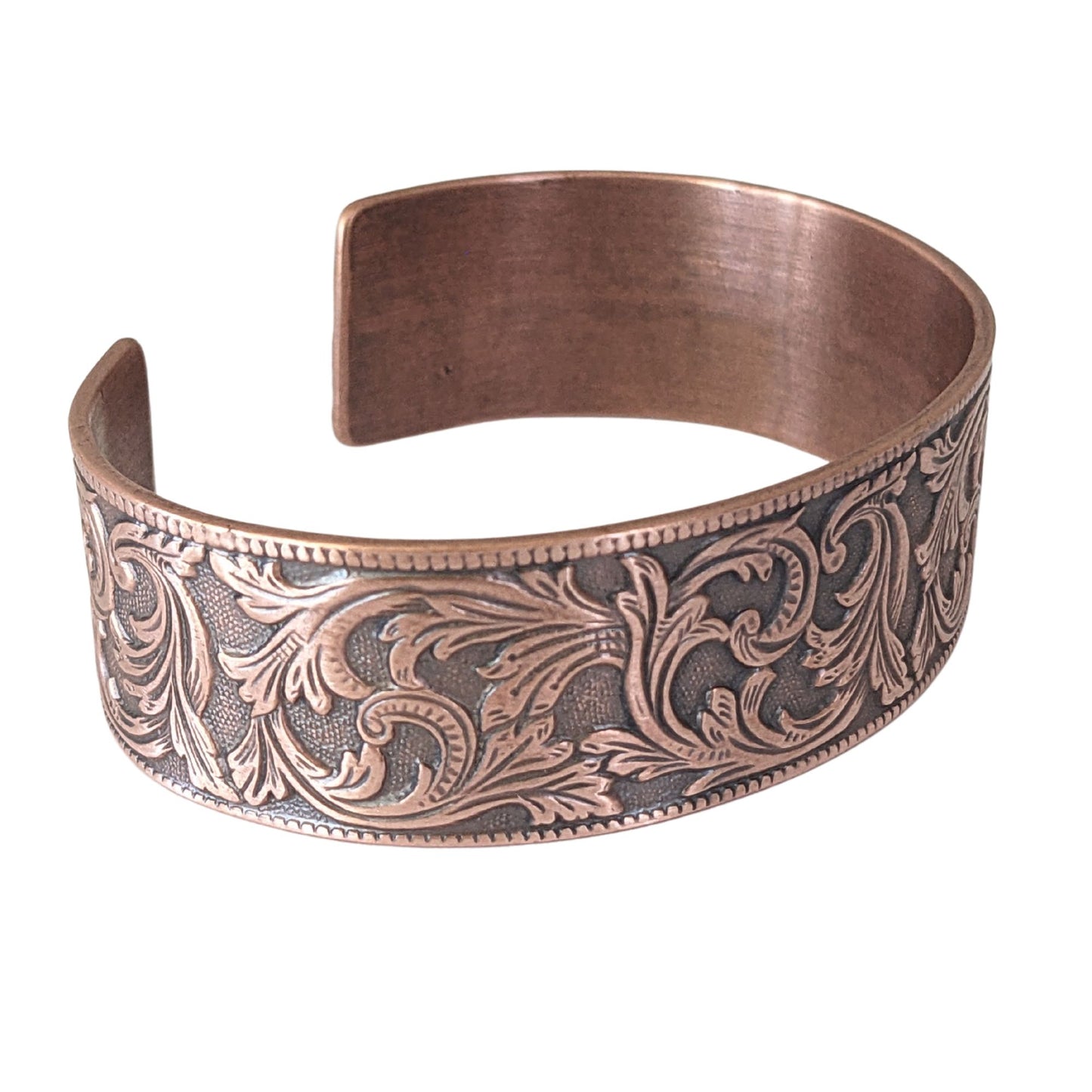 copper cuff bracelet with a repeating flourish leaf pattern on a spotted texture background.