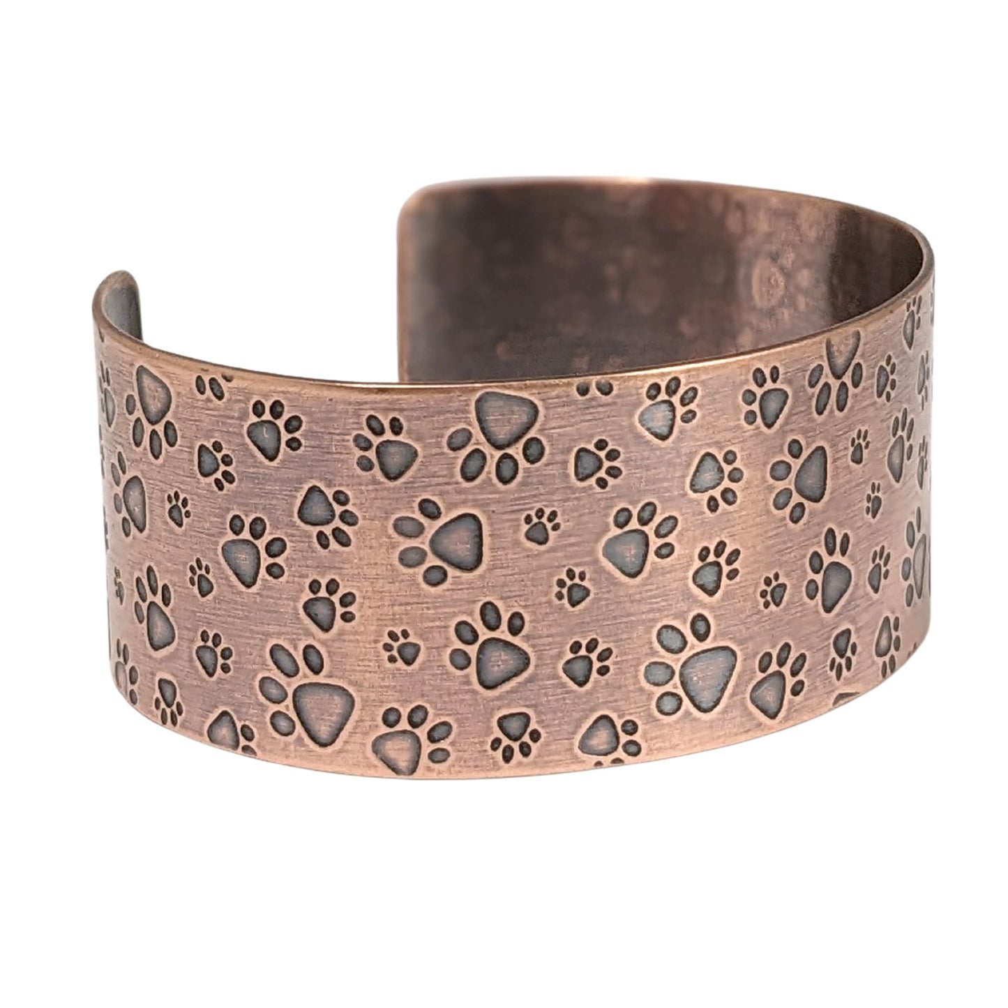 Copper cuff bracelet covered in a dog paw print design. The paw prints are in various sizes.