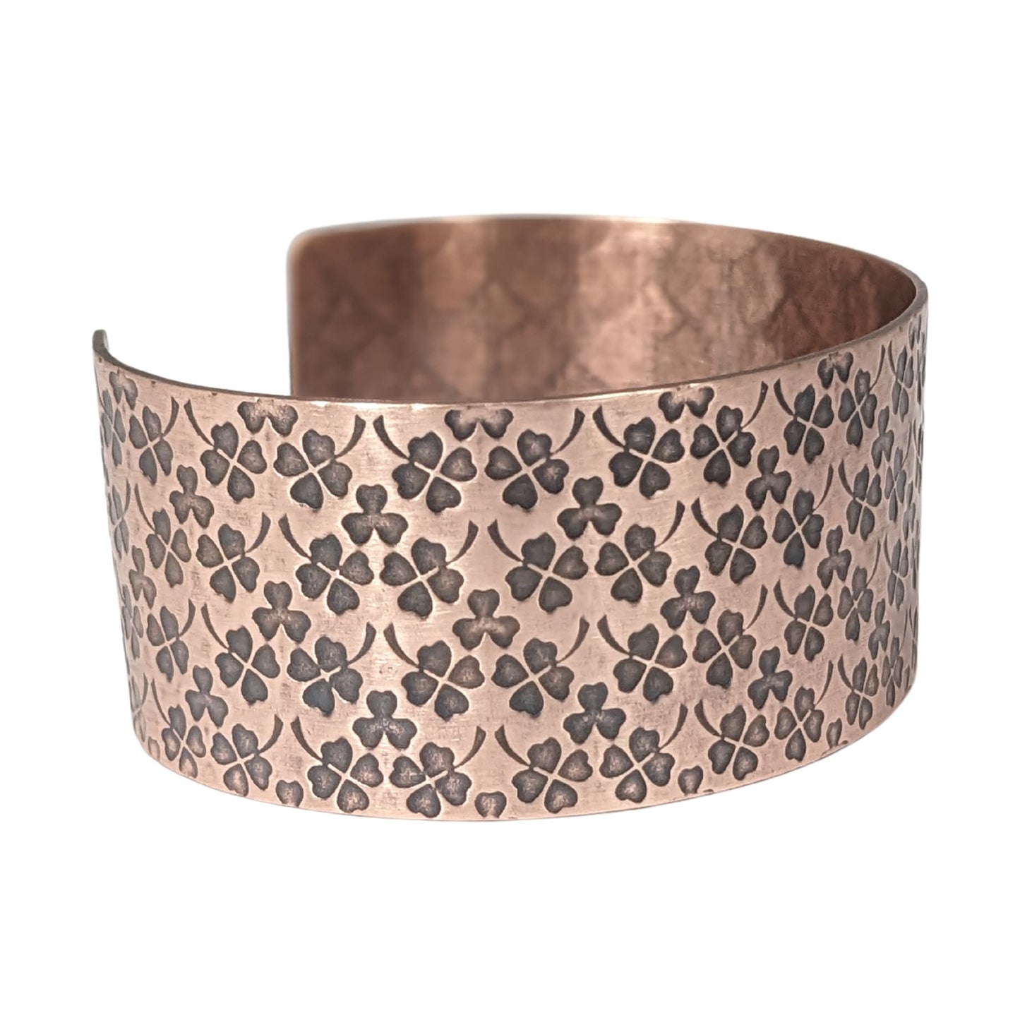 Copper cuff bracelet covered in impressions of small four leaf clovers.