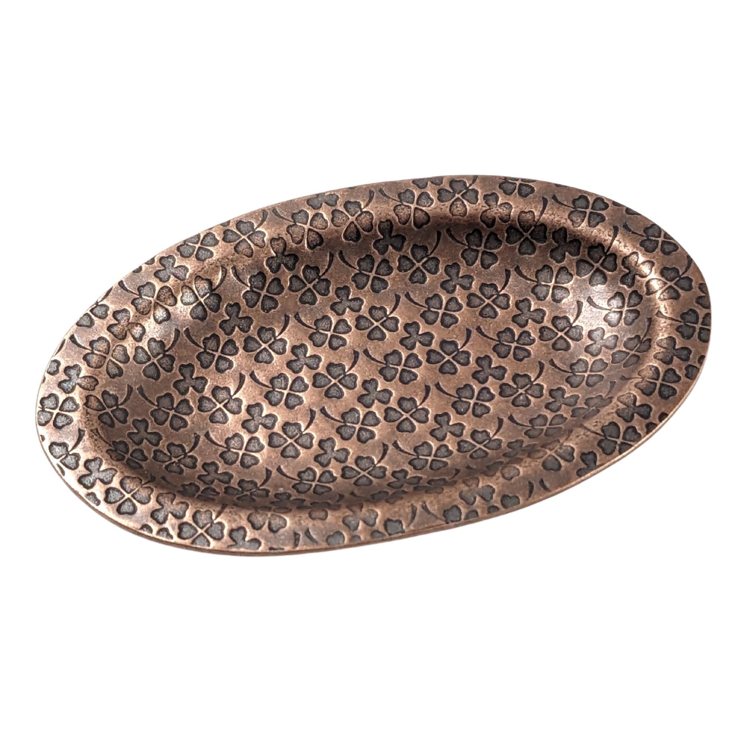 An oval copper ring dish with a raised edge. The dish has an impressed pattern of four leaf clovers.