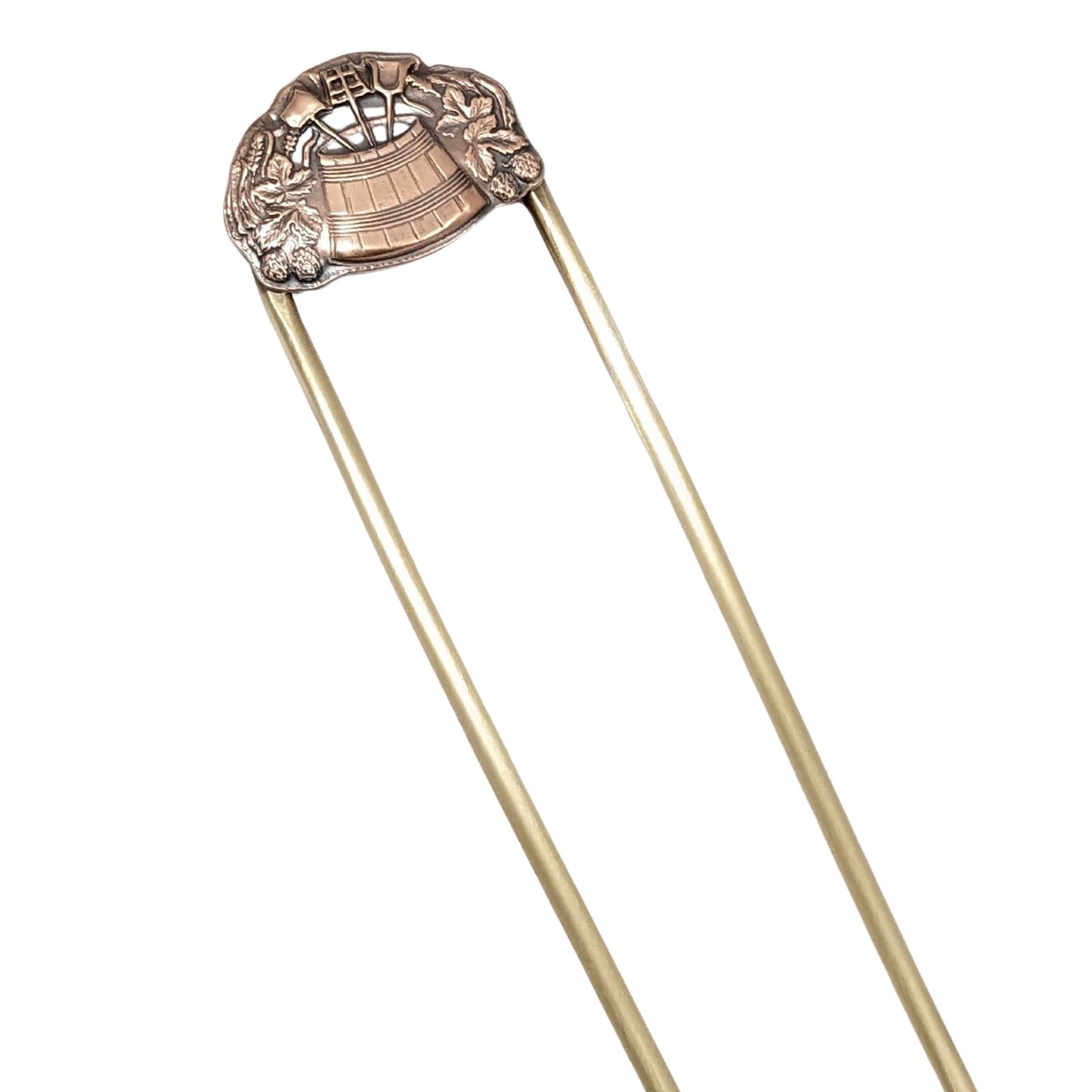 brass hair fork with a dimensional design in copper. The design has a wooden barrel in the middle, filled with three long handled garden tools. Surrounding the barrel are leaves and strawberries.