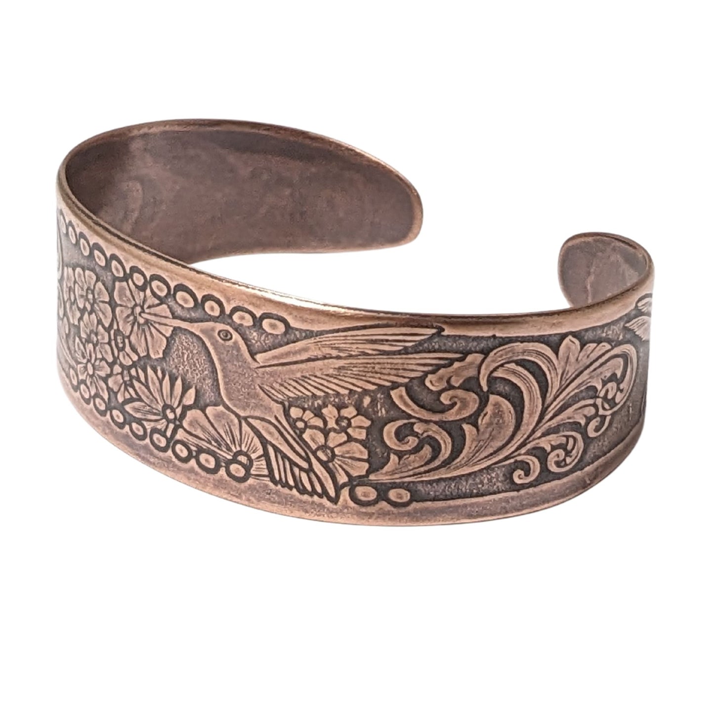 Tapered copper cuff bracelet. Pattern across middle is a hummingbird surrounded by flowers. At each end of the cuff there is a smaller hummingbird and flower.