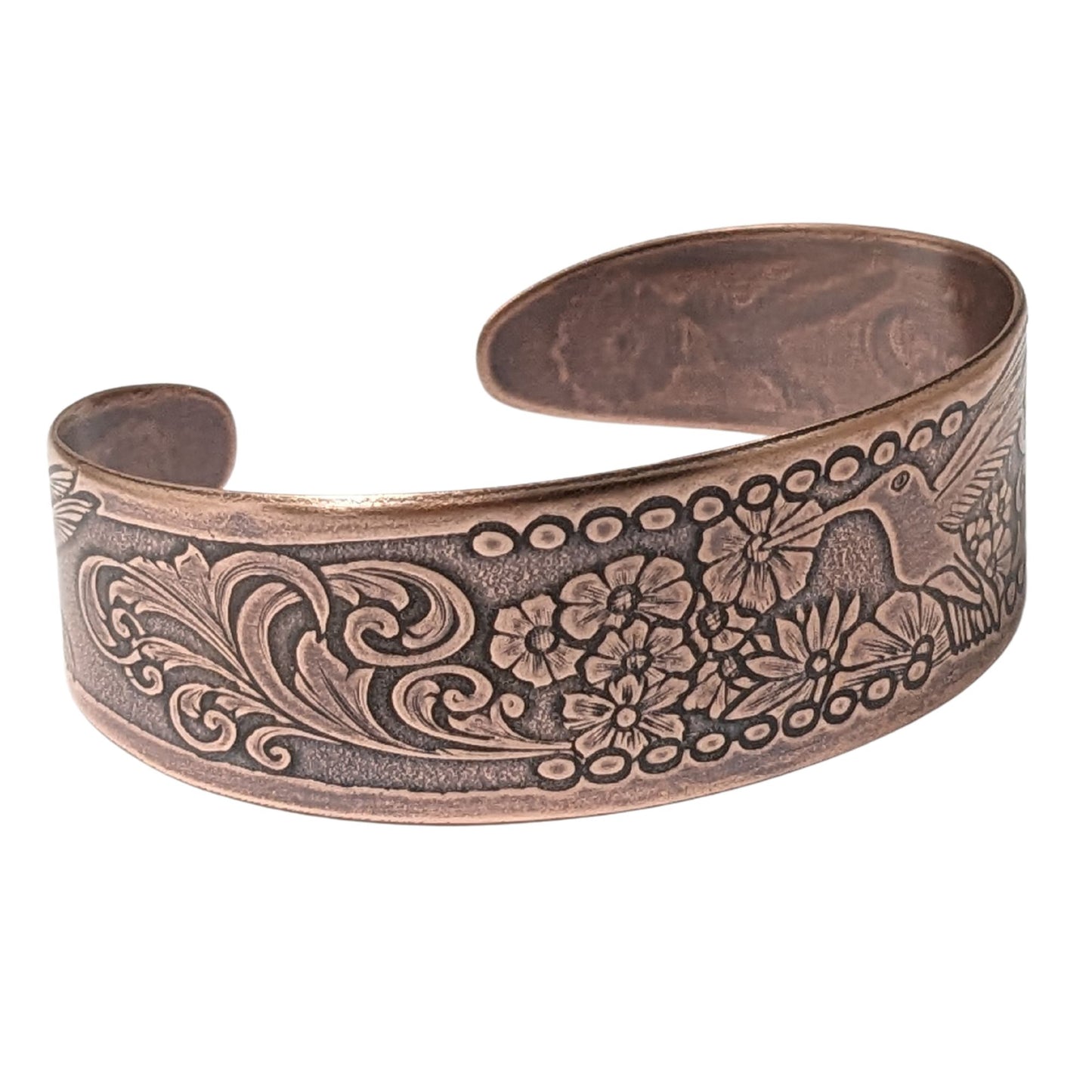 Tapered copper cuff bracelet. Pattern across middle is a hummingbird surrounded by flowers. At each end of the cuff there is a smaller hummingbird and flower.