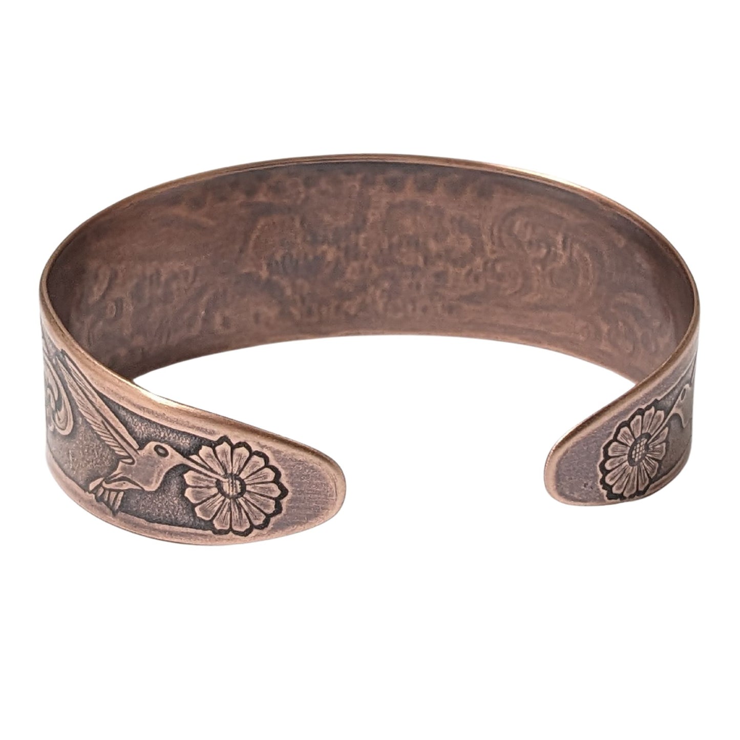 Tapered copper cuff bracelet. Pattern across middle is a hummingbird surrounded by flowers. At each end of the cuff there is a smaller hummingbird and flower.