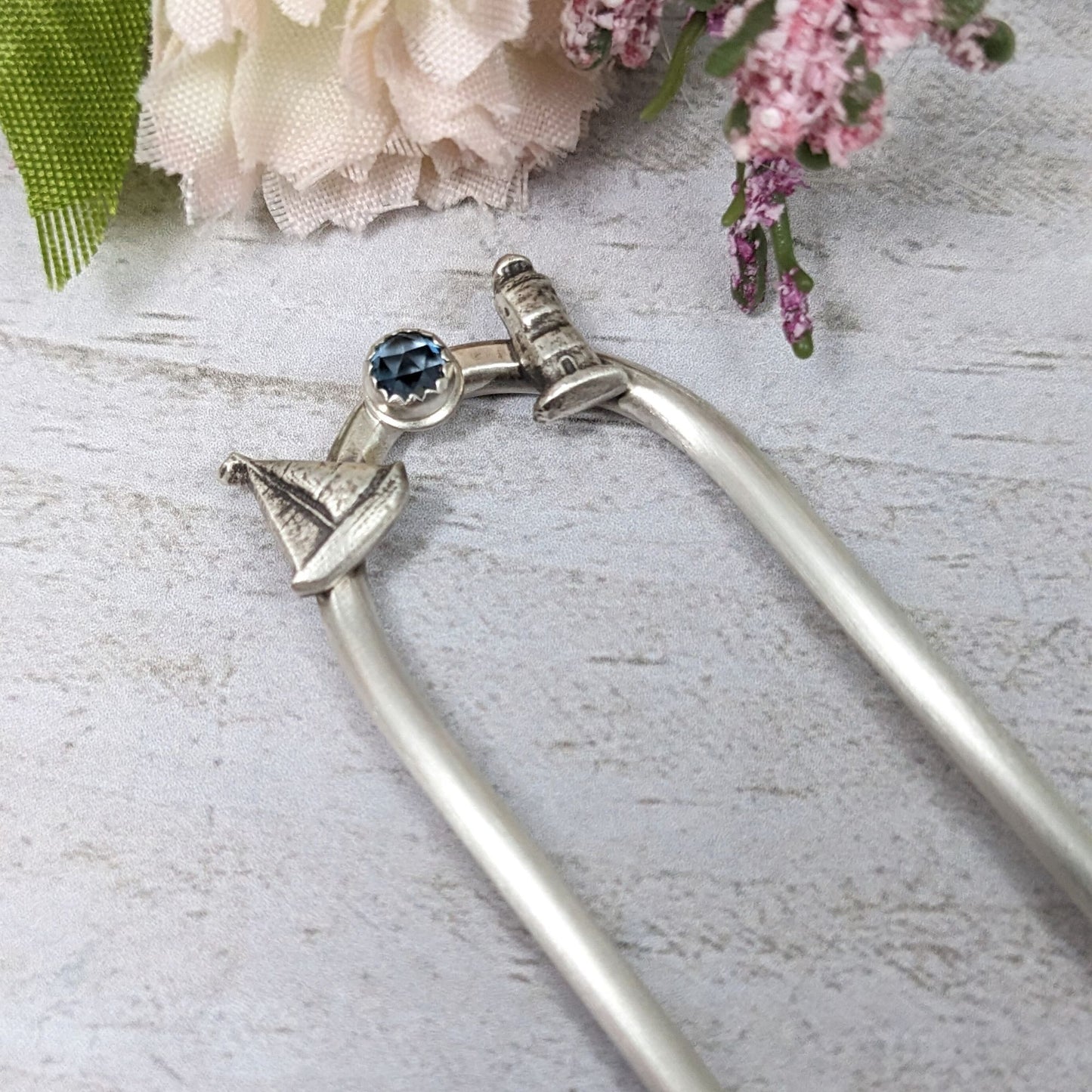 Sterling silver hair fork with three small design elements. Left is a silver sailboat, center is a rose cut blue topaz gemstone, right is a silver lighthouse