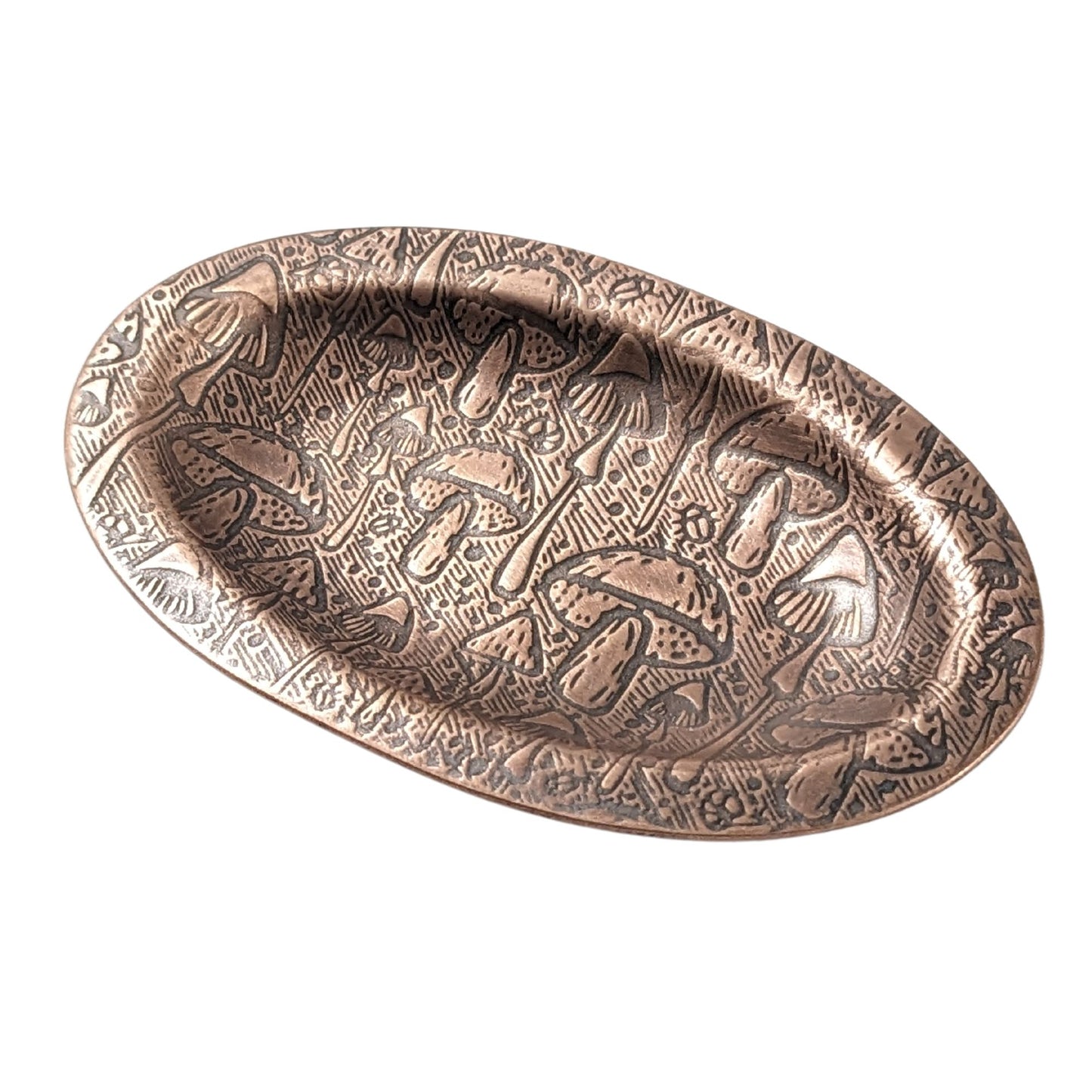 An oval copper ring dish with a raised edge. The dish has an impressed pattern of a variety of mushrooms