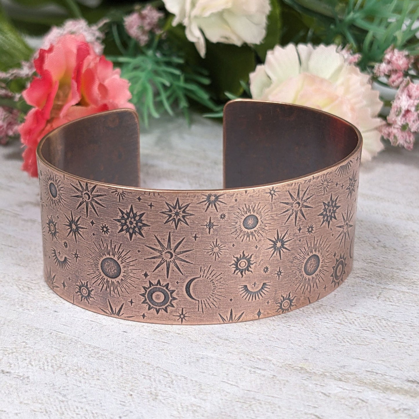A one inch wide copper cuff bracelet covered in an impressed design of stars and planets.