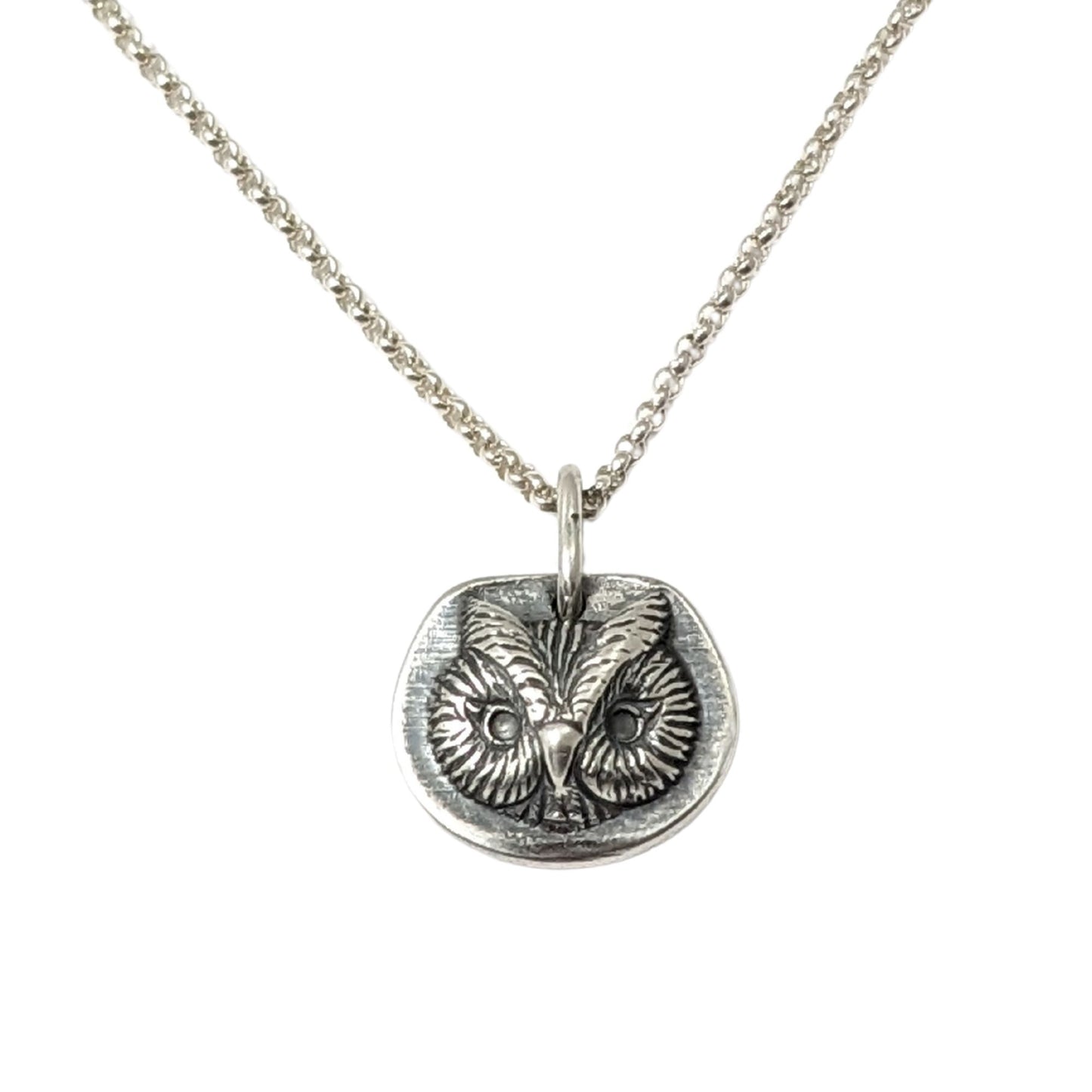 Sterling silver pendant of an owl face. The pendant is three dimensional and thick.