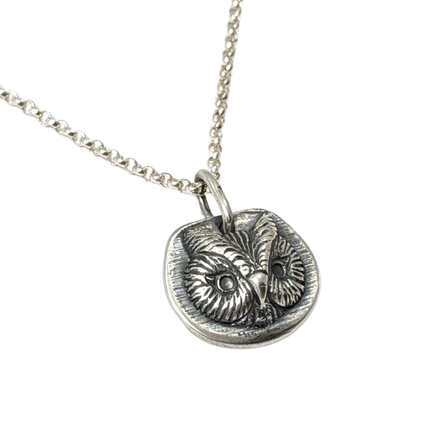 Sterling silver pendant of an owl face. The pendant is three dimensional and thick.
