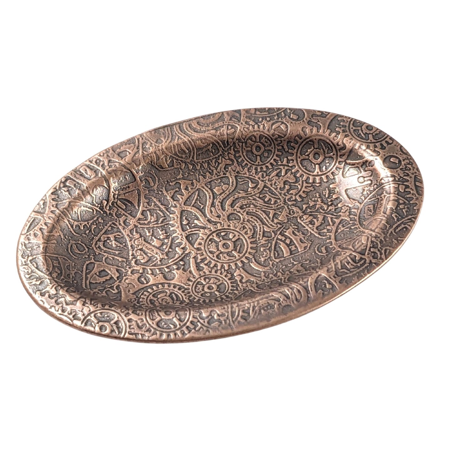 An oval copper ring dish with a raised edge. The dish has an impressed pattern of steampunk style gears and cogs.
