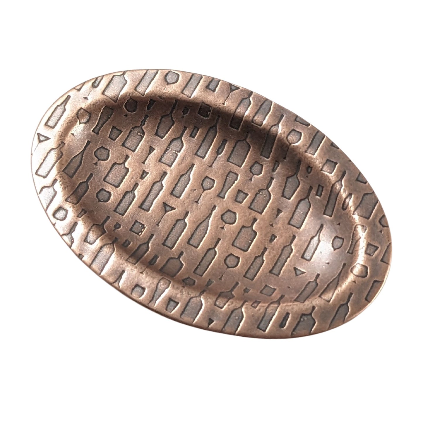 An oval copper ring dish with a raised edge. The dish has an impressed designs of wine and cocktail glasses plus wine and liquor bottles.
