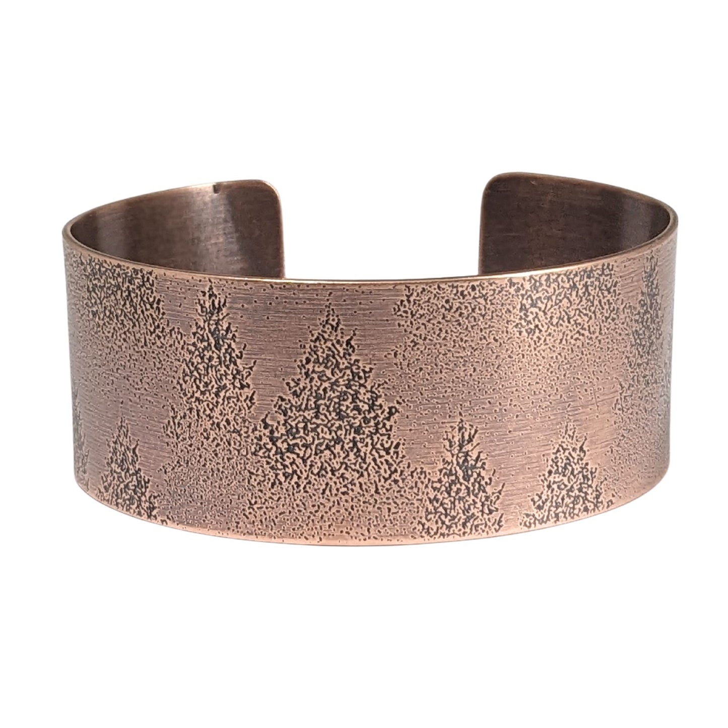 A copper cuff bracelet with an impressed design of fir tree evergreens in snow.