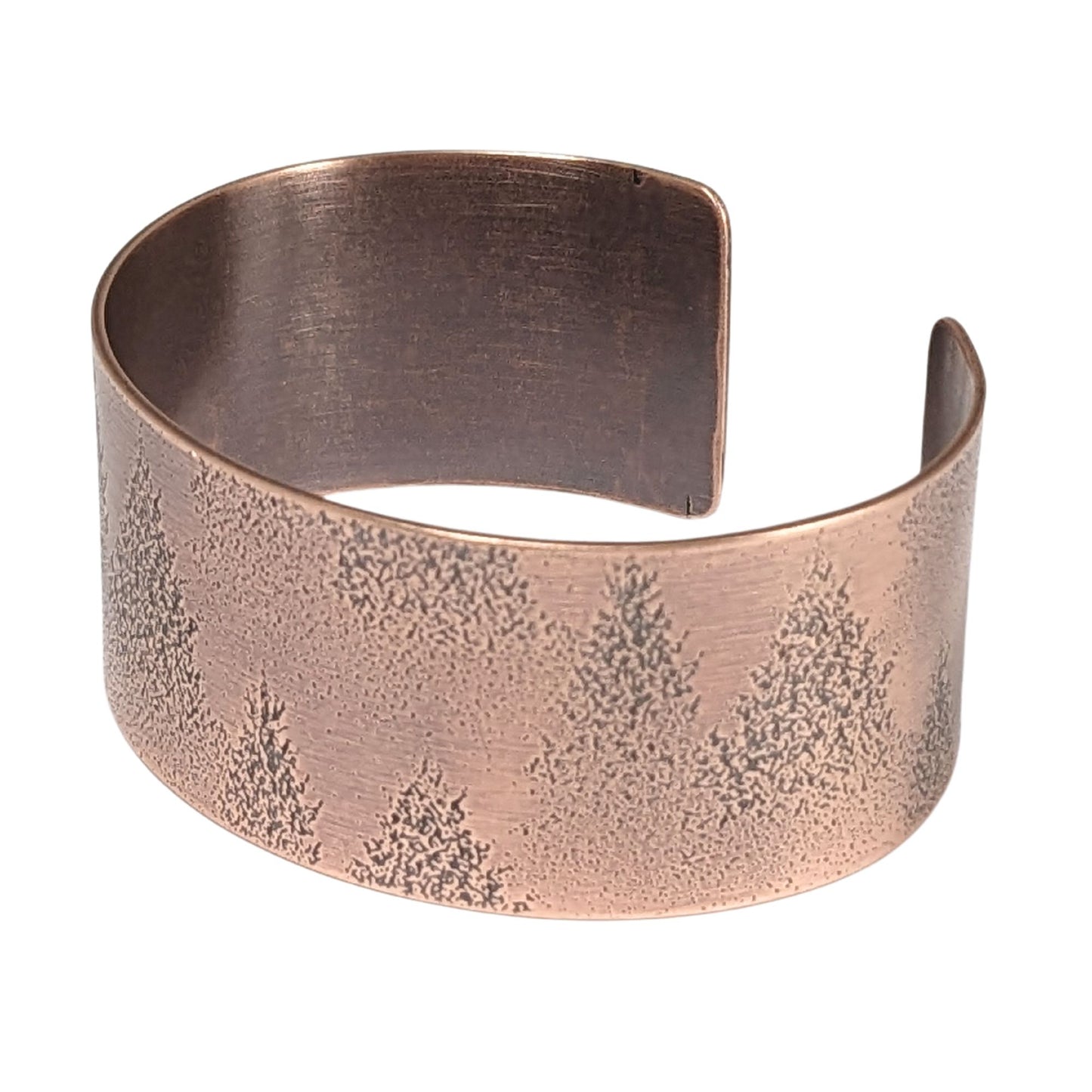 A copper cuff bracelet with an impressed design of fir tree evergreens in snow.
