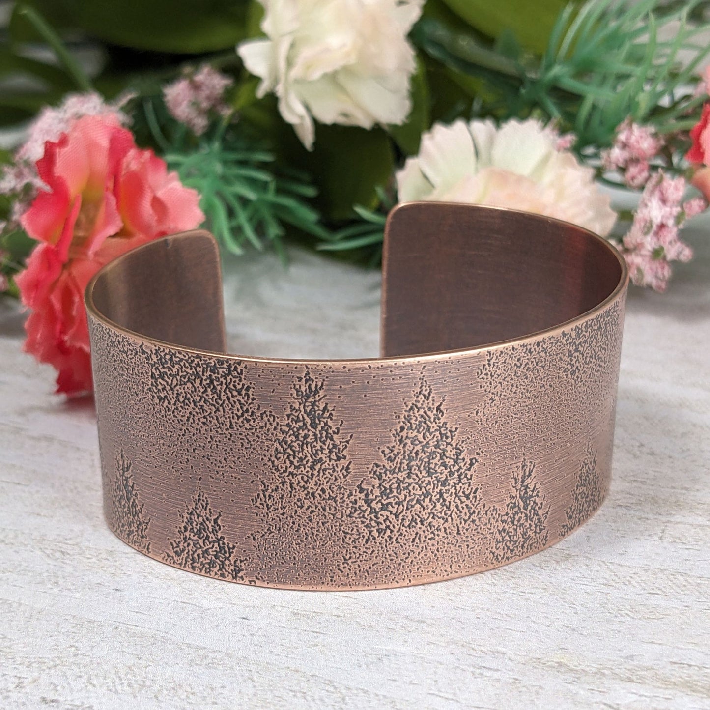 A copper cuff bracelet with an impressed design of fir tree evergreens in snow.