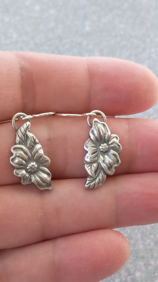 Video of stering silver dogwood earrings. The Design is asymmetric, the left earring has a leaf above the flower and the right earring has a leaf below the flower.