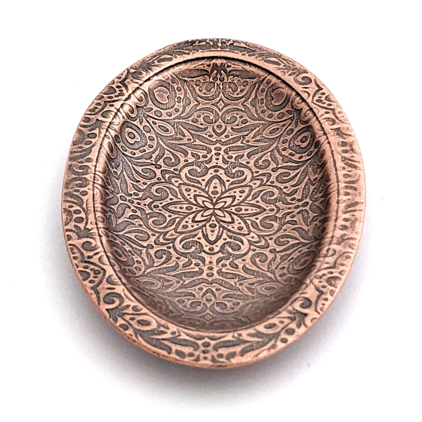 Copper oval ring dish with abstract garden flowers and leaves design. Dish is 2 inches by three inches with a raised lip.