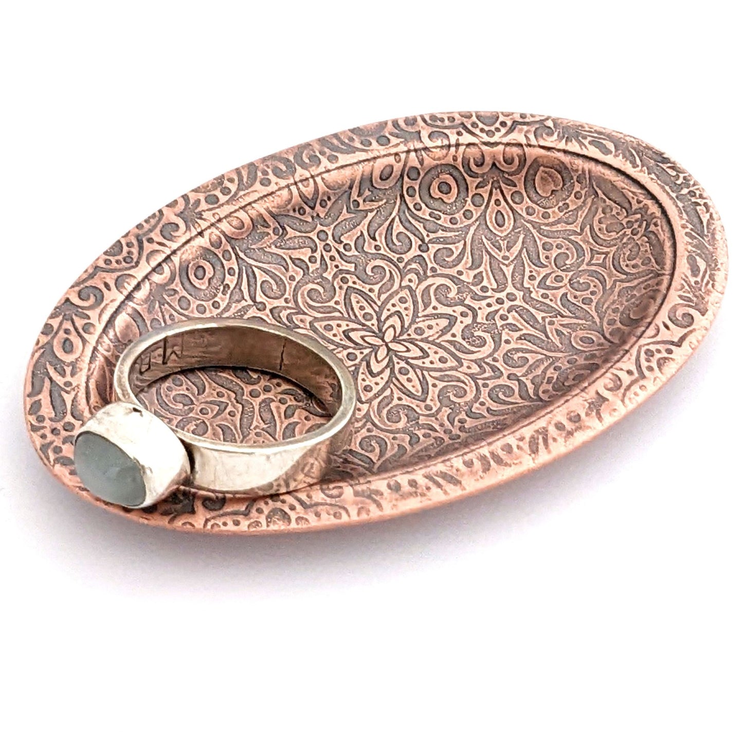 Copper oval ring dish with abstract garden flowers and leaves design. Dish is 2 inches by three inches with a raised lip.