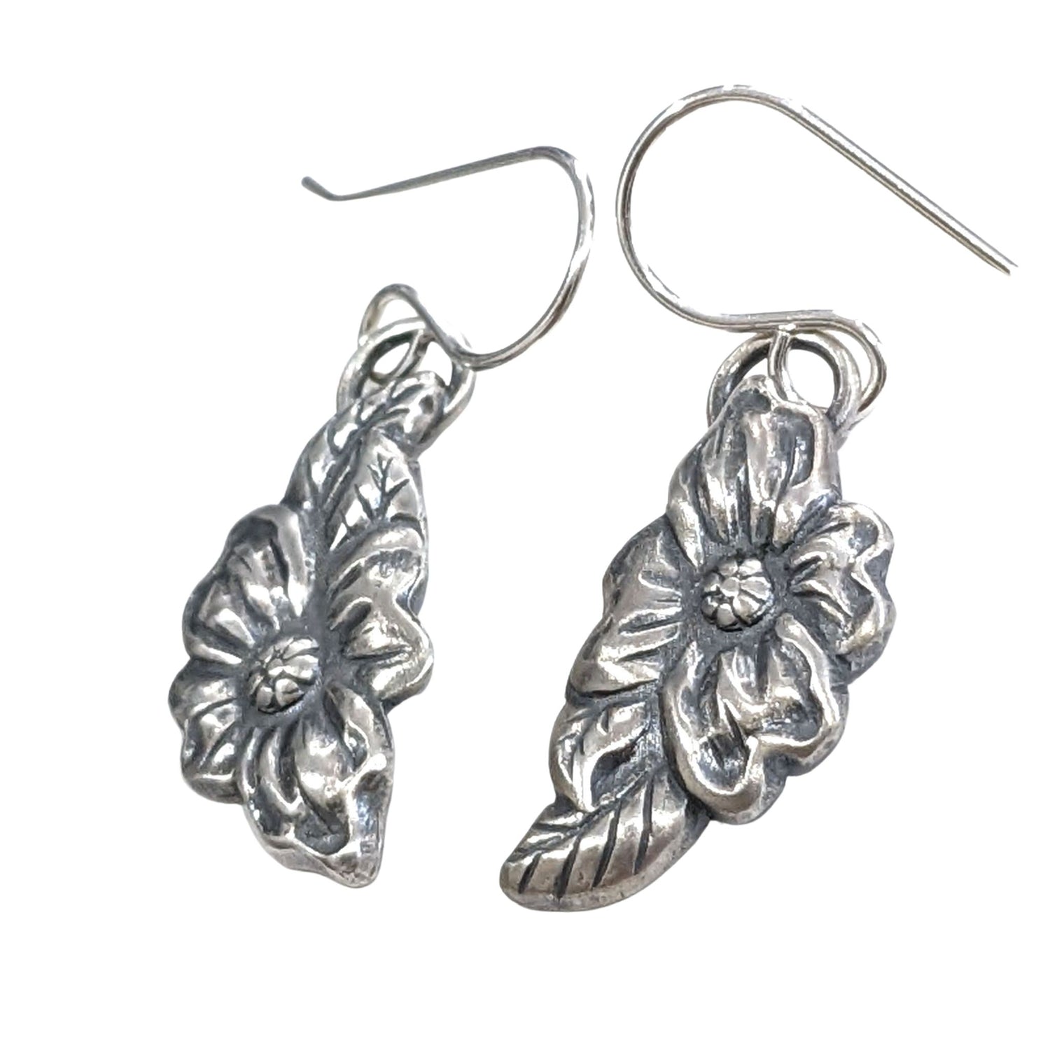 Stering silver dogwood flower earrings. The Design is asymmetric, the left earring has a leaf above the flower and the right earring has a leaf below the flower.