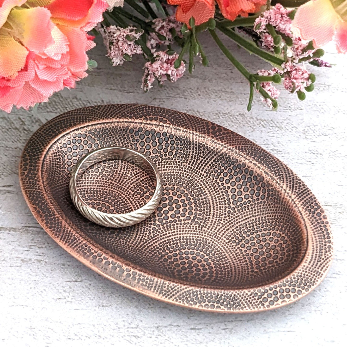 Copper oval ring dish with repeating pattern of dotted arches. Dish is 2 inches by three inches with a raised lip.