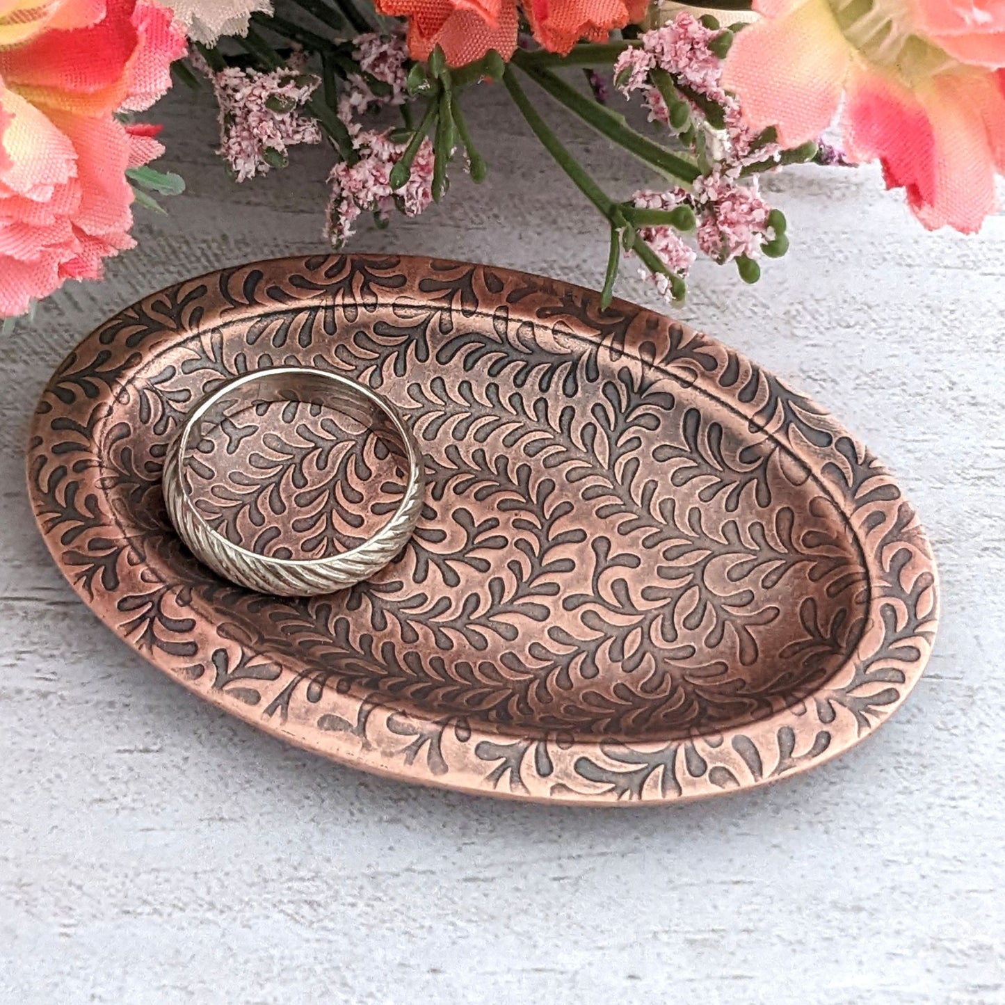 Copper oval ring dish with abstract fiddlehead fern pattern. Dish is 2 inches by three inches with a raised lip.