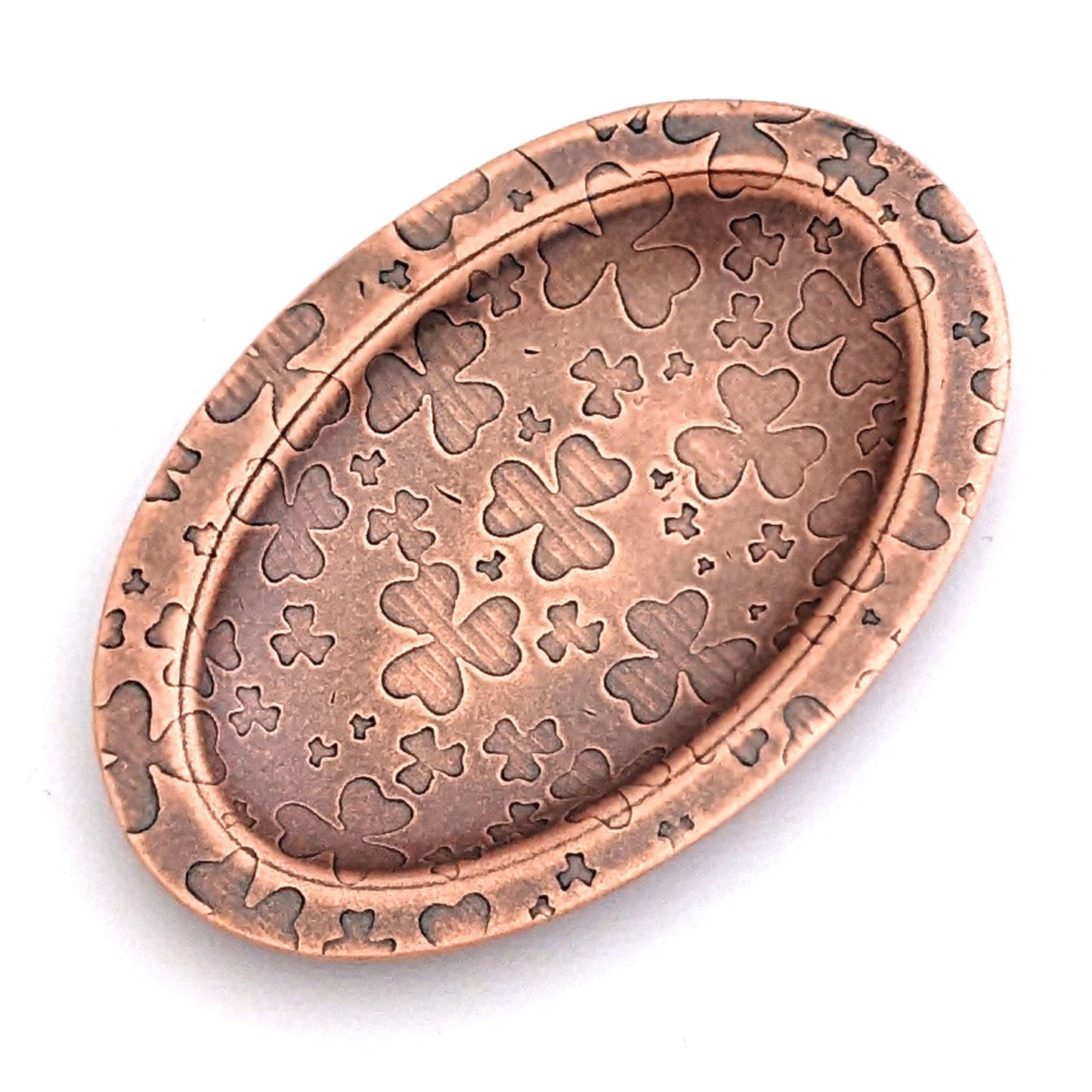 Copper oval ring dish with repeating pattern of shamrocks. Dish is 2 inches by three inches with a raised lip.