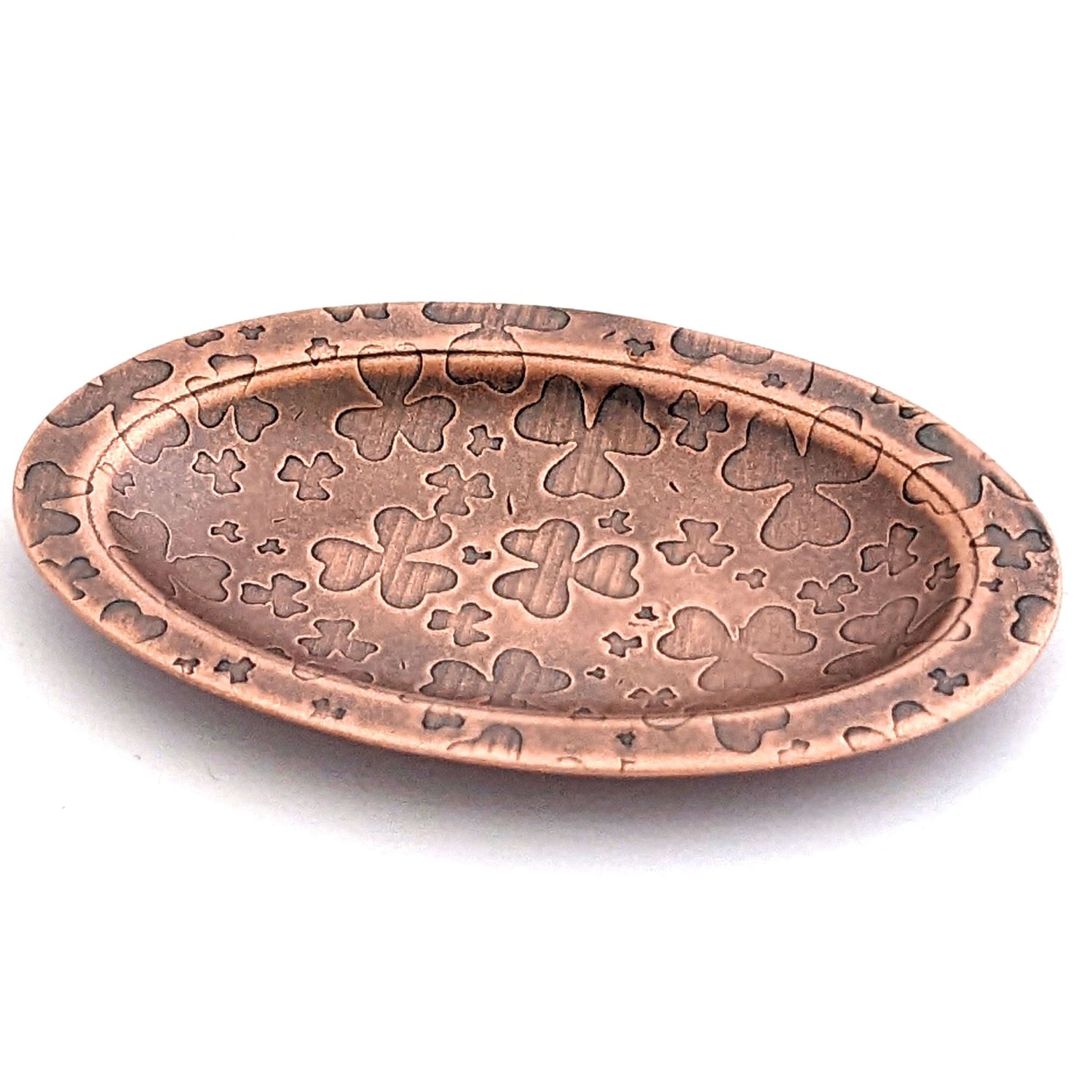Copper oval ring dish with repeating pattern of shamrocks.  Dish is 2 inches by three inches with a raised lip.