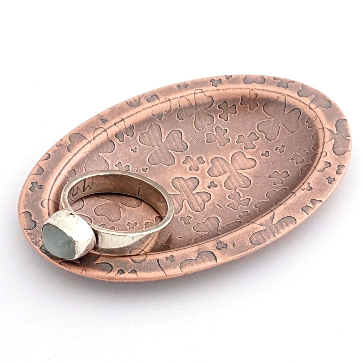 Copper oval ring dish with repeating pattern of shamrocks. Dish is 2 inches by three inches with a raised lip.