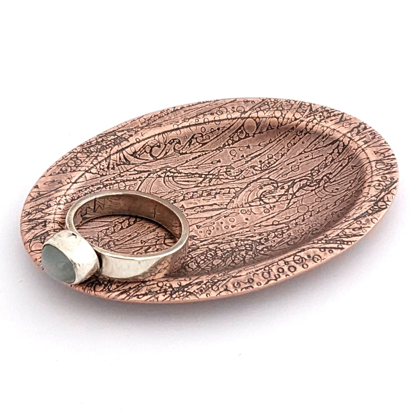 Copper oval ring dish with design of waves in a stormy sea. Dish is 2 inches by three inches with a raised lip.
