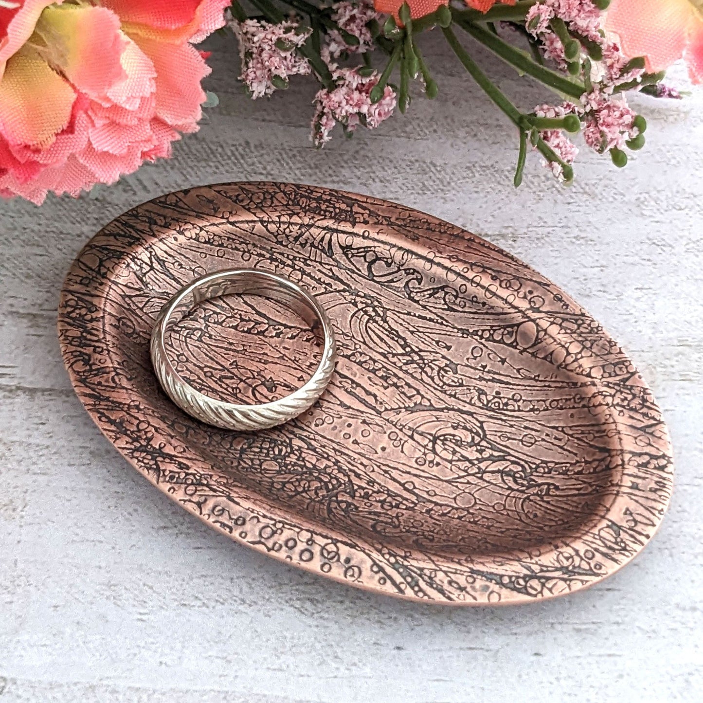Copper oval ring dish with design of waves in a stormy sea. Dish is 2 inches by three inches with a raised lip.