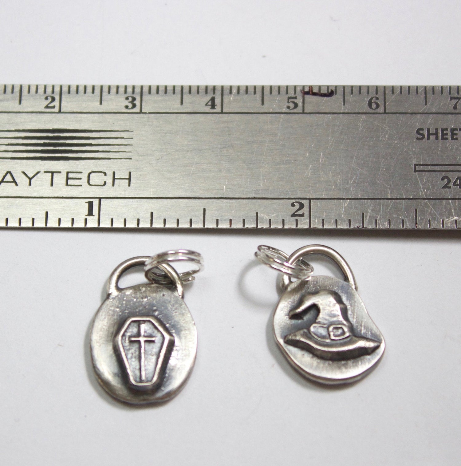 Sterling silver coffin and witches hat charms shown with ruler for scale.