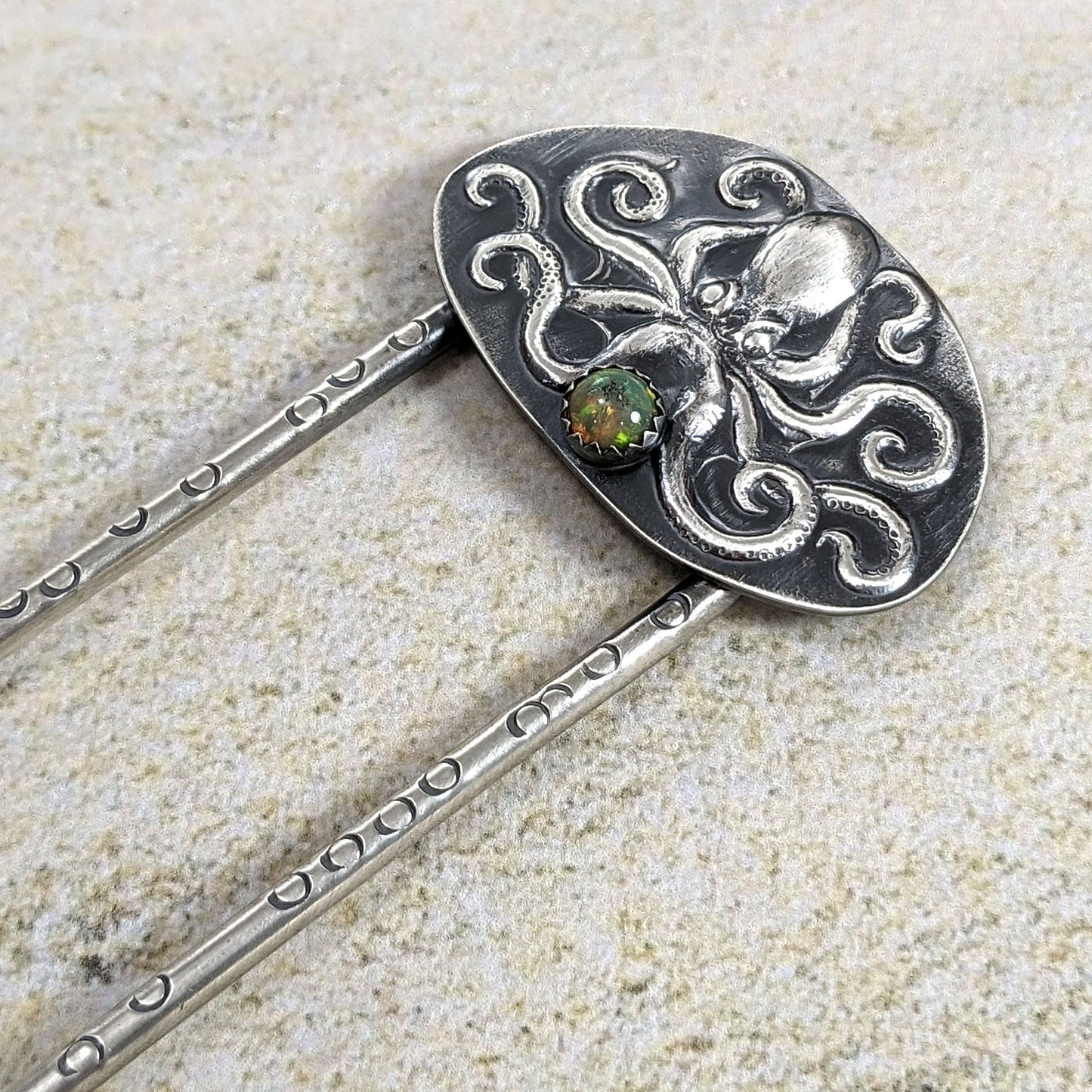 Octopus sterling silver hair fork. The octopus is a detailed raised design on a sterling silver sheet. There is a flashy 5mm opal below the octopus. The fork has stamped circles to represent octopus suckers.  fork and octopus design are blackened to show the details. The entire piece is handmade sterling silver.