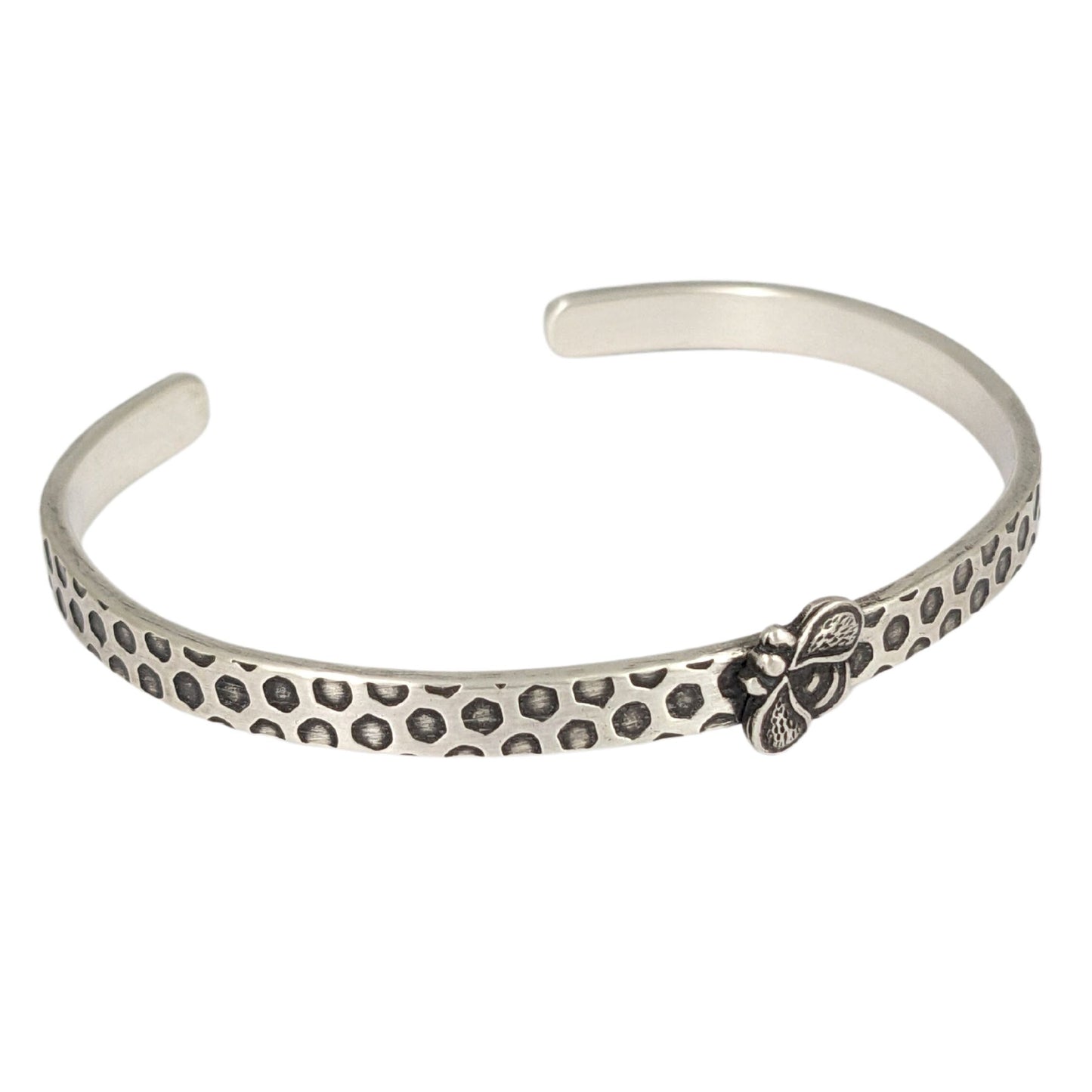 Narrow sterling silver cuff bracelet with a hexagon honeycomb pattern. A the center of the cuff there's a sterling silver honeybee.