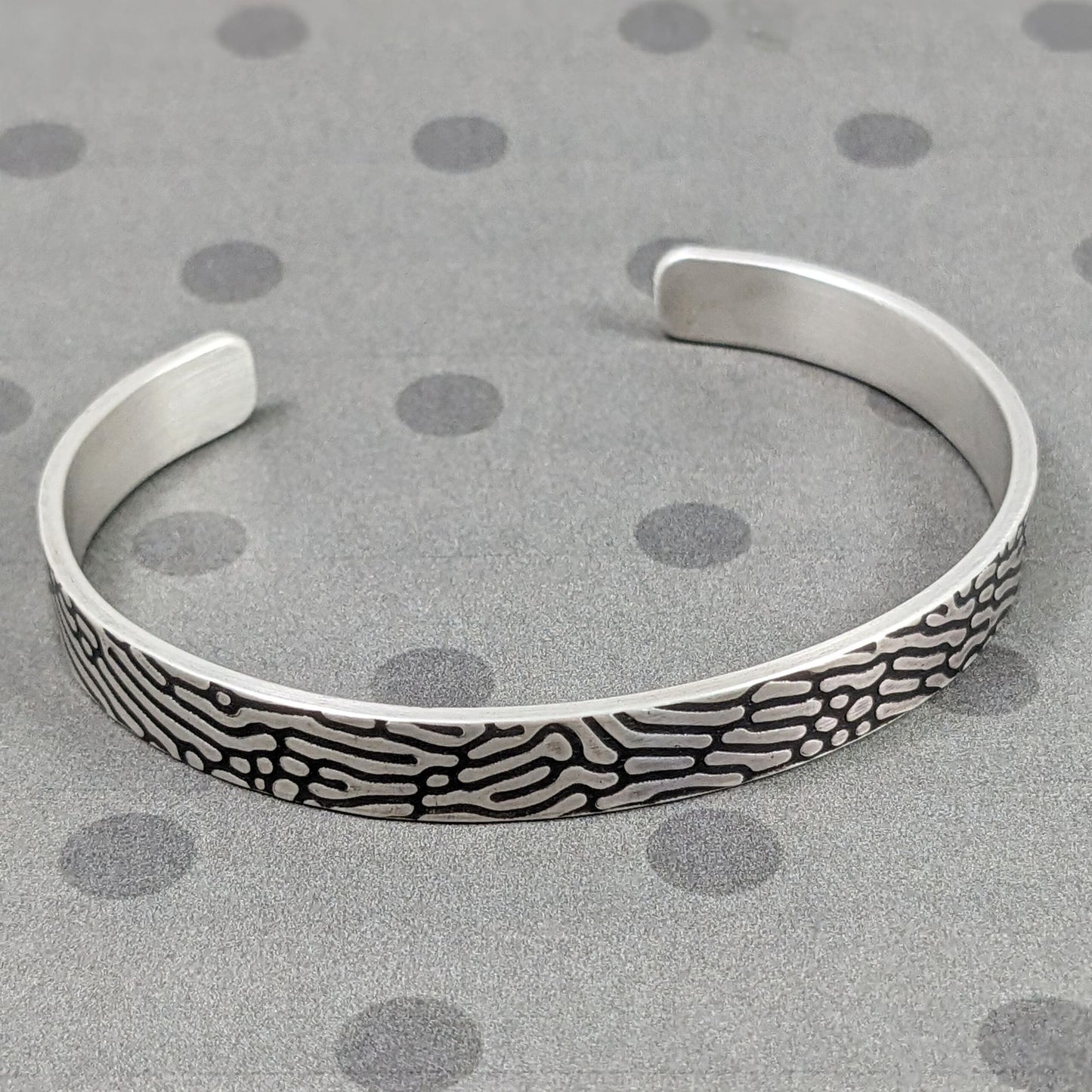 Rectangular shaped sterling silver wire cuff bracelet with an impressed design that looks like Brain Coral. The impressed design is darkened, so the coral lines are black against the silver.