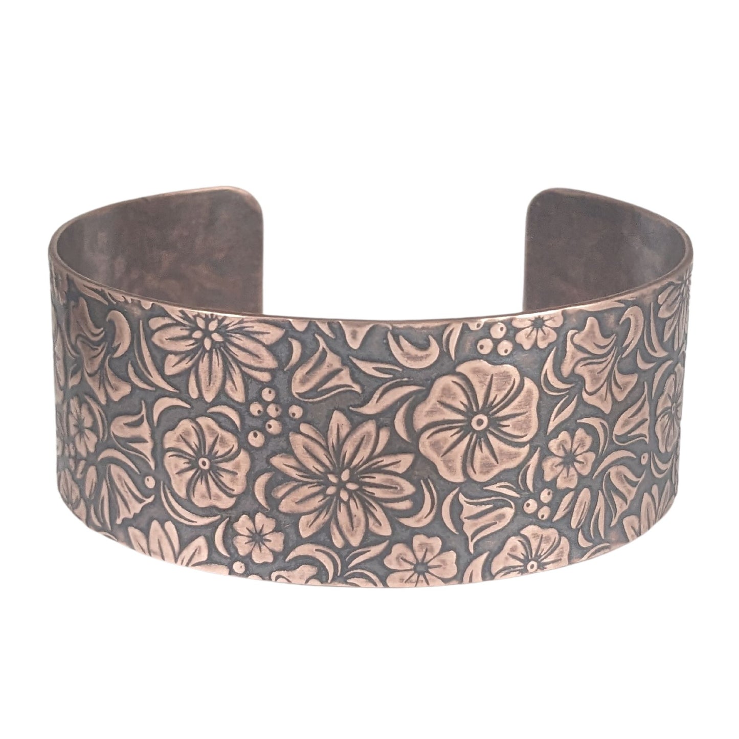 One inch wide copper cuff bracelet covered in designs of common garden flowers, looked at from above. The background around the flowers is darkened to accentuate the detail.