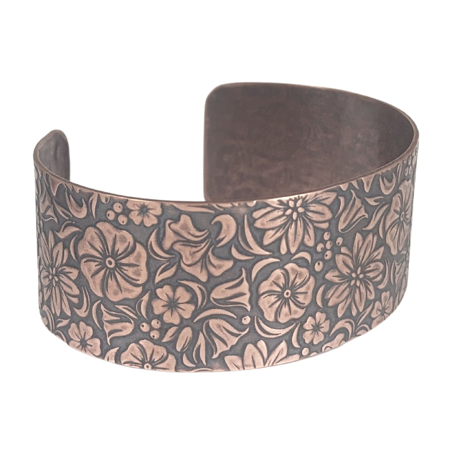 One inch wide copper cuff bracelet covered in designs of common garden flowers, looked at from above. The background around the flowers is darkened to accentuate the detail.