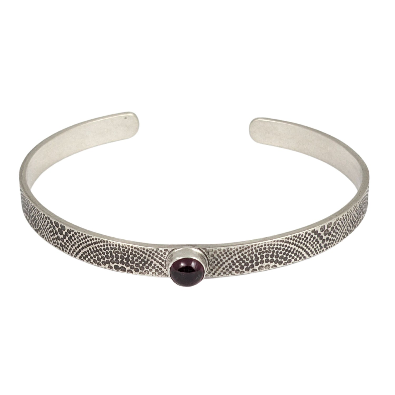 Narrow sterling silver cuff bracelet. The silver is covered with an arch pattern. In the center is a red garnet gemstone.