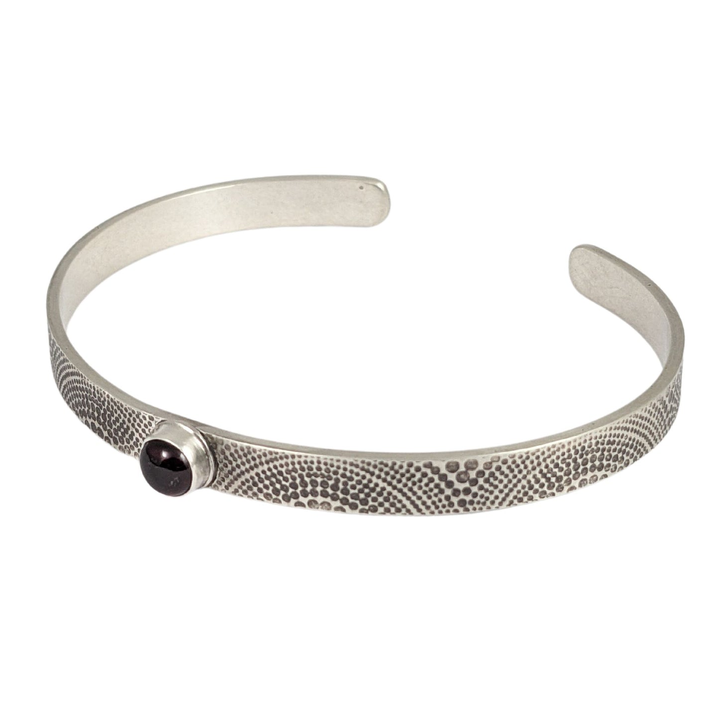 Narrow sterling silver cuff bracelet. The silver is covered with an arch pattern. In the center is a red garnet gemstone.