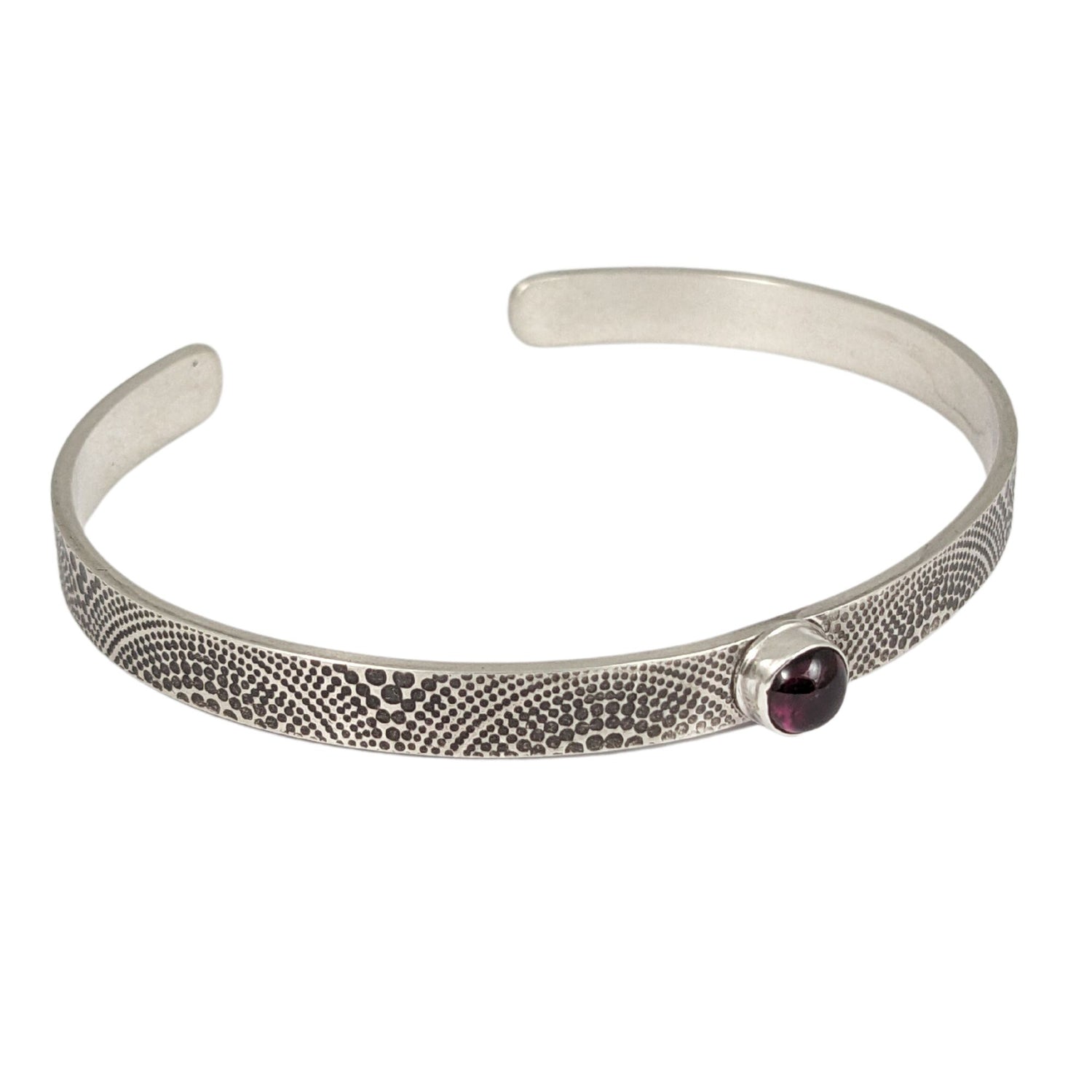 Narrow sterling silver cuff bracelet. The silver is covered with an arch pattern. In the center is a red garnet gemstone.
