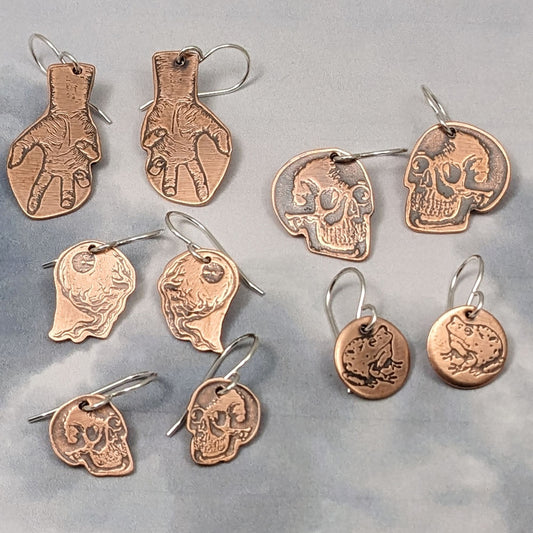 Copper earrings with halloween designs. hands, skulls, brains, and frogs